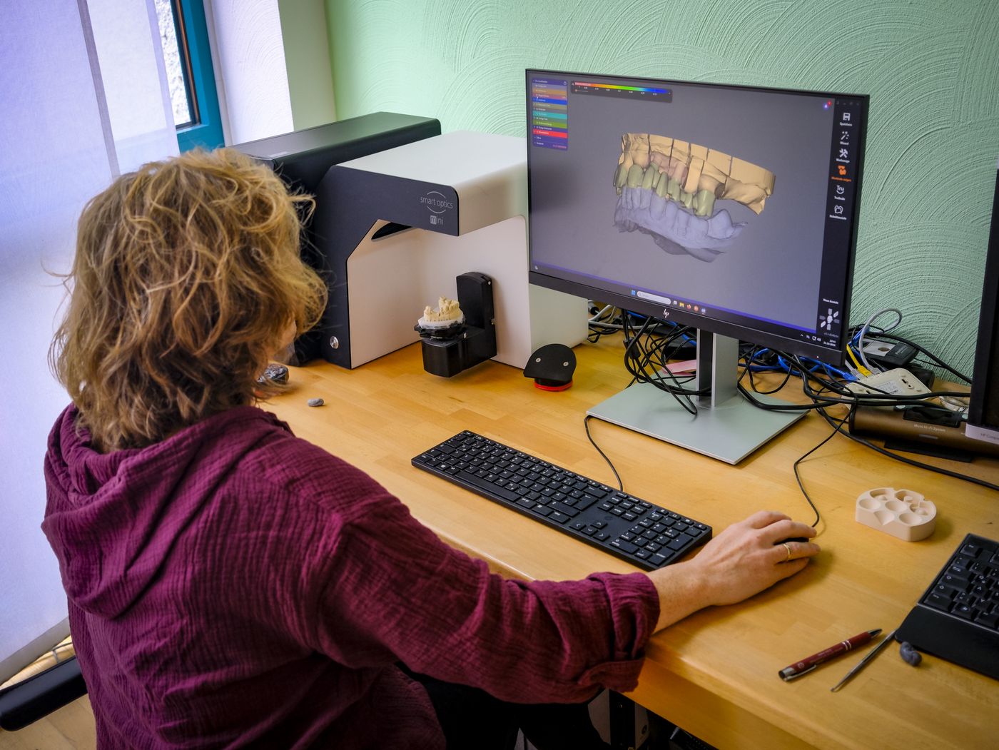 Zahntechnikerin konstruiert eine Brücke am CAD-Bildschirm, daneben der Laborscanner