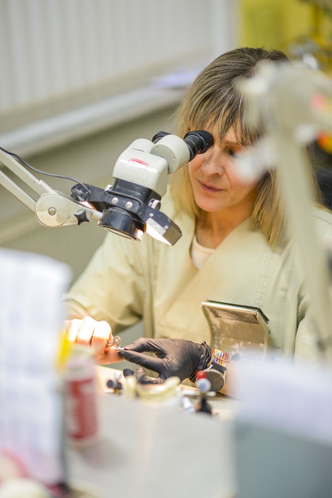 Zahntechnikerin kontrolliert eine Arbeit unter dem Mikroskop