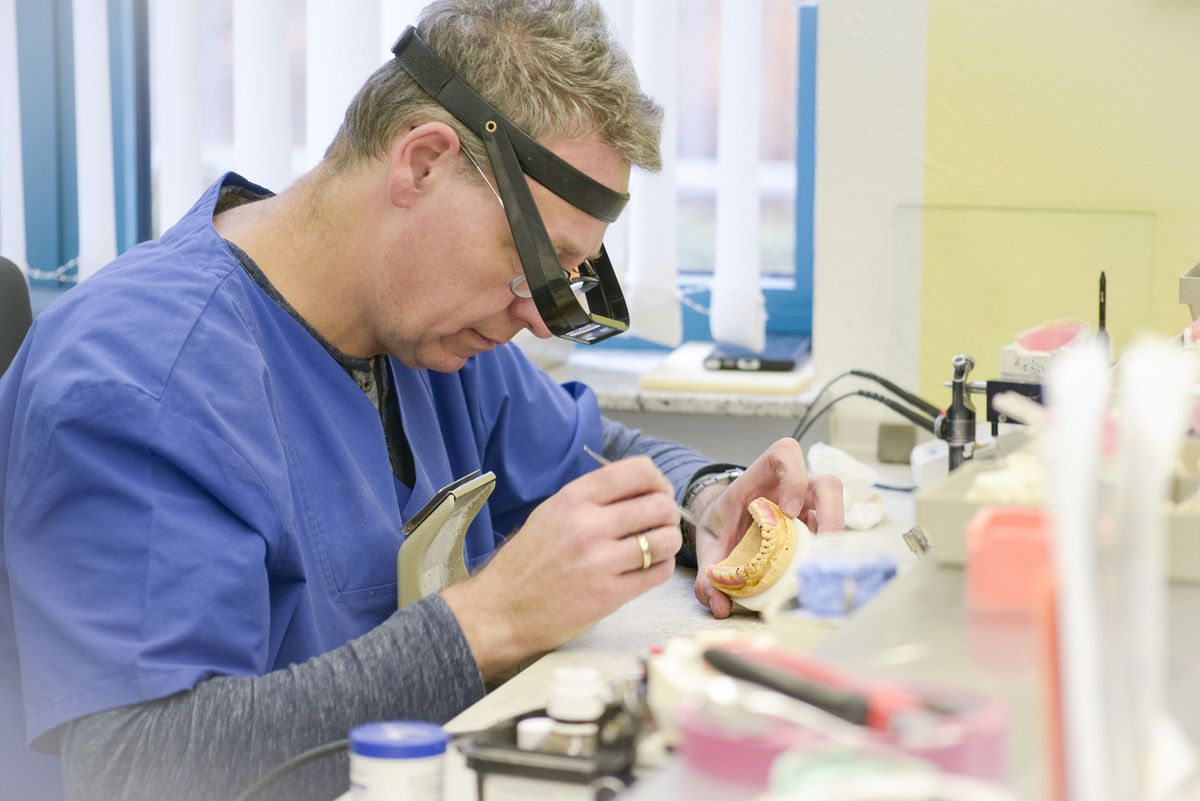 Zahntechniker mit Lupenbrille bei der Arbeit an einer Kunststoff- und Modellgussarbeit
